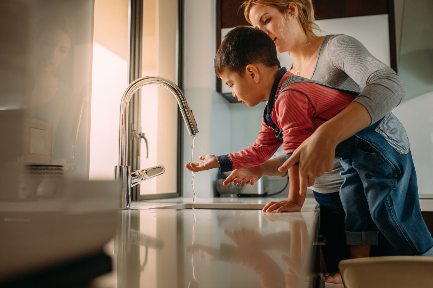 Little boy with mother washing hands in kitchen sink